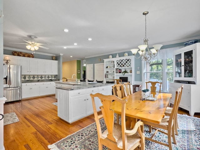 dining space with ceiling fan with notable chandelier, sink, light hardwood / wood-style flooring, and ornamental molding