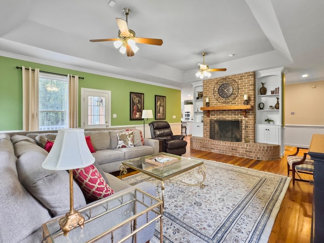 living room with a raised ceiling, wood-type flooring, a fireplace, and ceiling fan