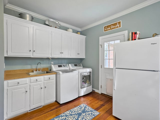 clothes washing area featuring separate washer and dryer, cabinets, sink, ornamental molding, and light hardwood / wood-style flooring