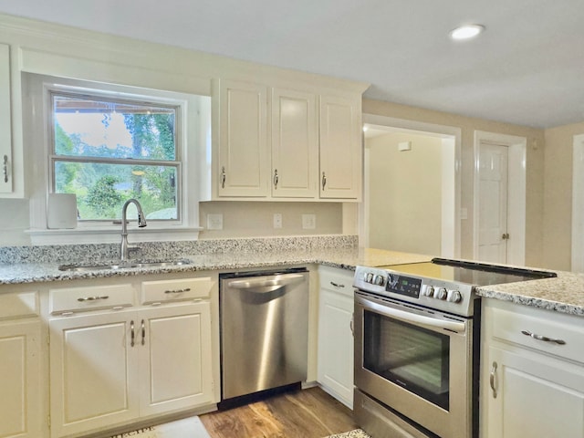 kitchen with appliances with stainless steel finishes, white cabinets, light stone counters, and sink