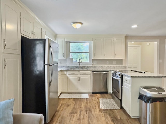 kitchen with sink, light wood-type flooring, appliances with stainless steel finishes, white cabinets, and light stone counters