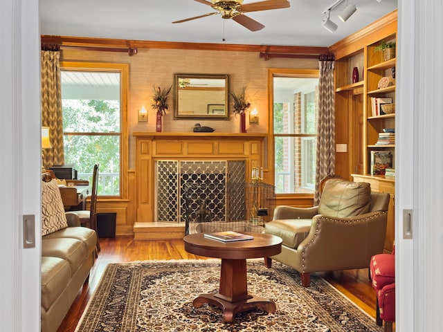 living area with a fireplace, ceiling fan, built in features, ornamental molding, and hardwood / wood-style flooring