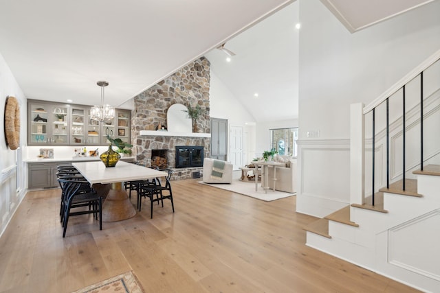 dining room featuring built in features, light hardwood / wood-style flooring, high vaulted ceiling, a notable chandelier, and a stone fireplace