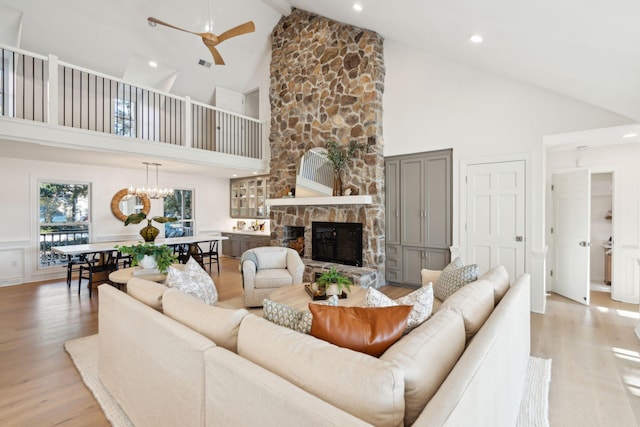 living room with beamed ceiling, high vaulted ceiling, a fireplace, light hardwood / wood-style flooring, and ceiling fan with notable chandelier