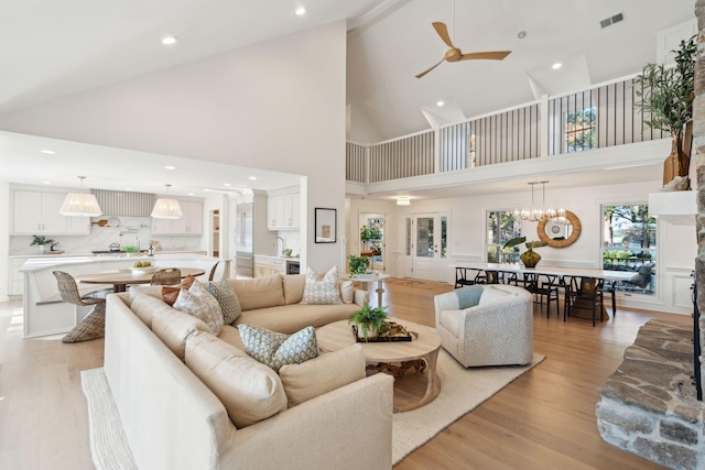 living room featuring light hardwood / wood-style floors, high vaulted ceiling, and ceiling fan with notable chandelier