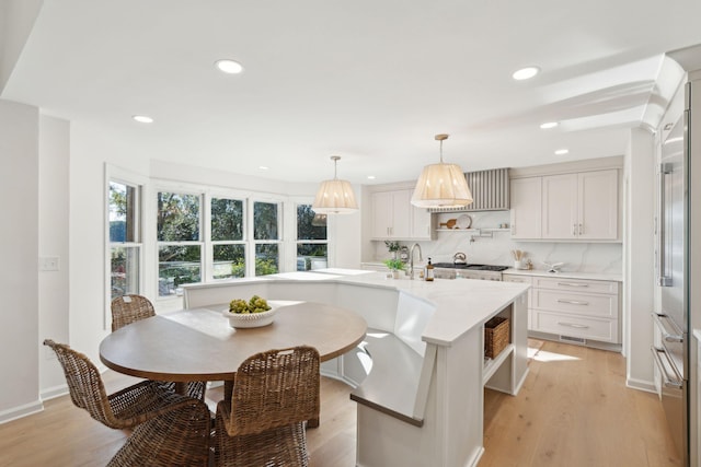 kitchen featuring white cabinetry, light wood-type flooring, tasteful backsplash, an island with sink, and pendant lighting