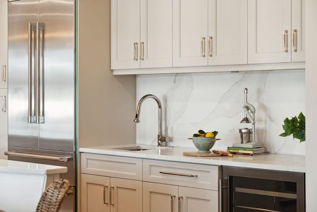 bar with white cabinets, wine cooler, stainless steel built in refrigerator, decorative backsplash, and sink