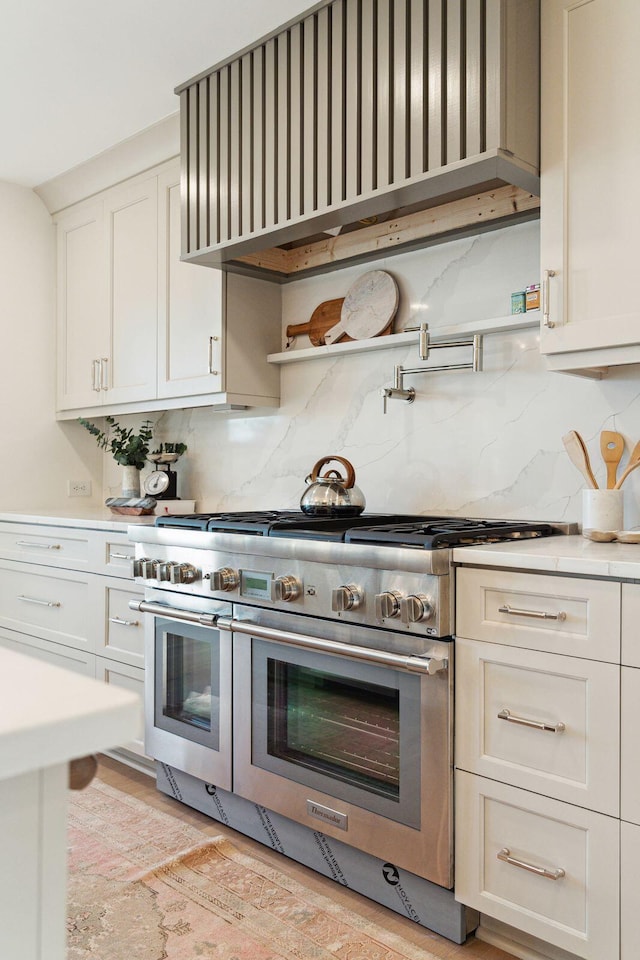 kitchen with white cabinets, wall chimney range hood, double oven range, and backsplash