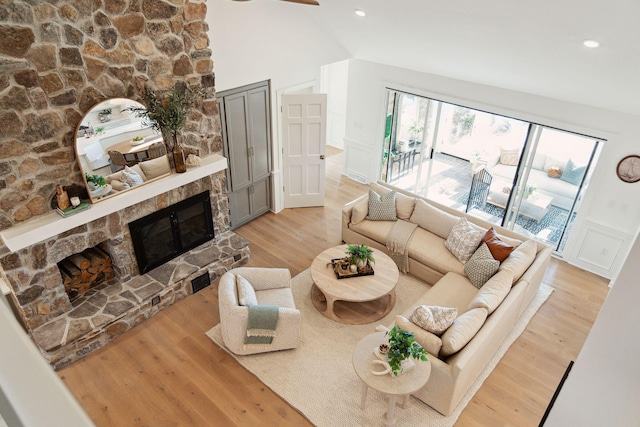 living room featuring light wood-type flooring, vaulted ceiling, and a stone fireplace