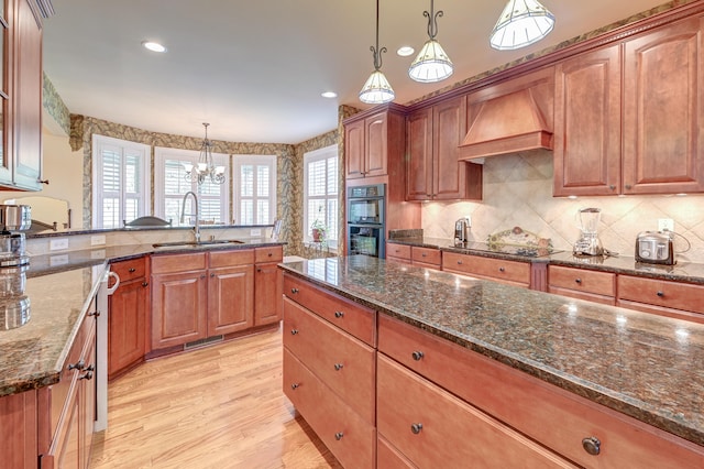 kitchen with premium range hood, light hardwood / wood-style flooring, hanging light fixtures, and sink