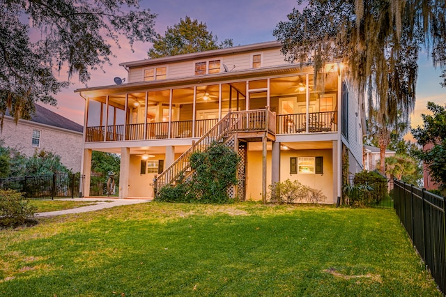 back house at dusk with a sunroom and a lawn