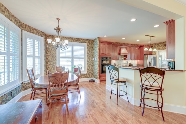 dining area featuring sink, light wood-type flooring, and an inviting chandelier