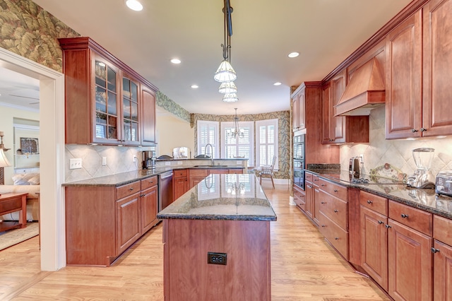 kitchen with light wood-type flooring, custom range hood, pendant lighting, dark stone countertops, and a kitchen island