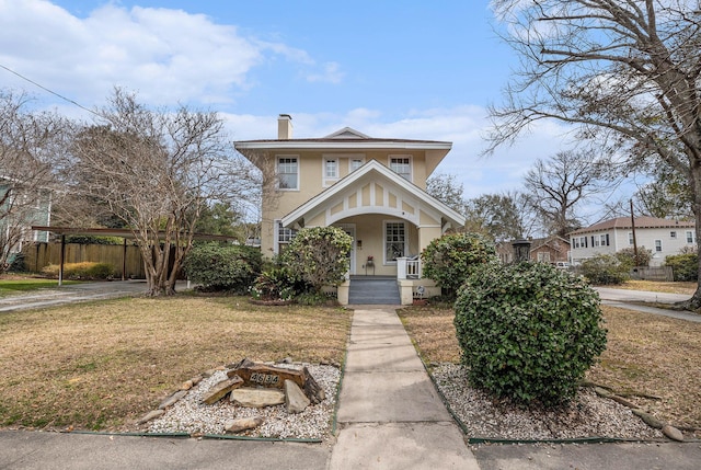 view of front facade featuring a chimney, stucco siding, a porch, fence, and a front lawn