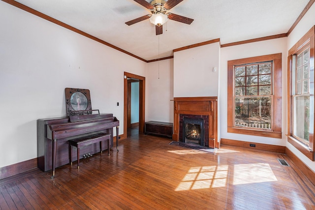 living area with visible vents, baseboards, wood-type flooring, a fireplace with flush hearth, and crown molding