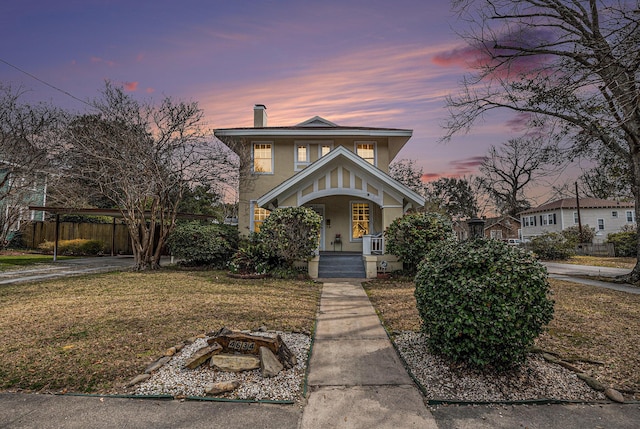 view of front facade with a porch, fence, stucco siding, a front lawn, and a chimney