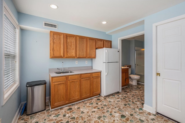 kitchen with a sink, visible vents, light countertops, freestanding refrigerator, and brown cabinetry