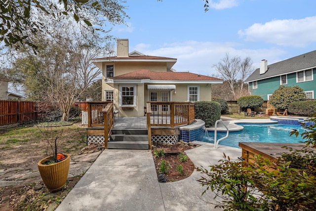 rear view of property featuring a fenced in pool, a fenced backyard, a chimney, a deck, and stucco siding