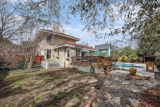 rear view of property featuring an outdoor pool, fence, a wooden deck, stucco siding, and a chimney