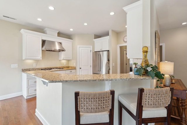 kitchen with visible vents, wall chimney exhaust hood, appliances with stainless steel finishes, a peninsula, and light wood-type flooring