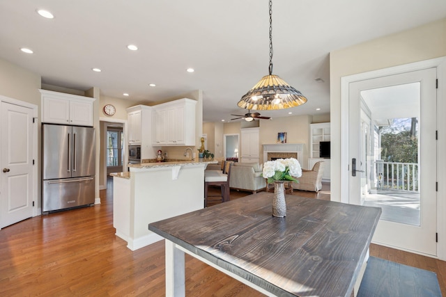 kitchen featuring stainless steel appliances, wood finished floors, white cabinets, light stone countertops, and a peninsula