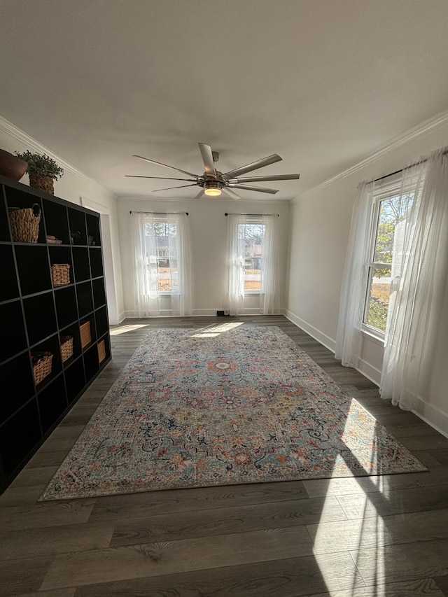 interior space featuring a ceiling fan, crown molding, baseboards, and dark wood-type flooring