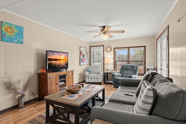 living room featuring ceiling fan, ornamental molding, a textured ceiling, and light wood-type flooring