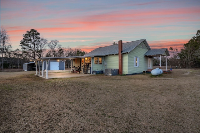 back house at dusk featuring a garage, central AC unit, and a lawn