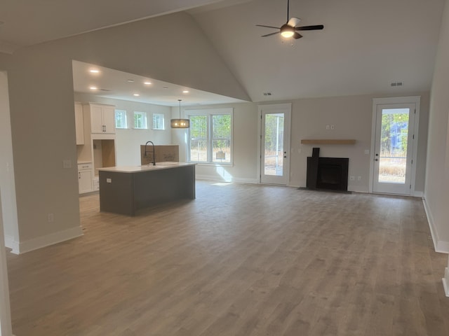 unfurnished living room featuring vaulted ceiling, ceiling fan, a wealth of natural light, and light hardwood / wood-style floors