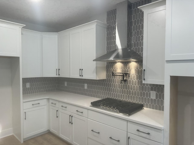 kitchen featuring tasteful backsplash, stainless steel gas cooktop, wall chimney range hood, and white cabinetry