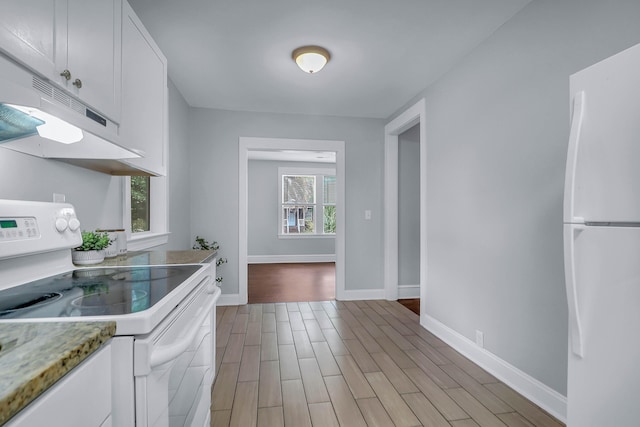 kitchen featuring white appliances, under cabinet range hood, white cabinets, light wood-type flooring, and baseboards