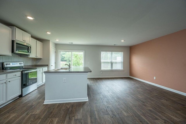 kitchen with white cabinets, an island with sink, appliances with stainless steel finishes, tasteful backsplash, and dark hardwood / wood-style flooring