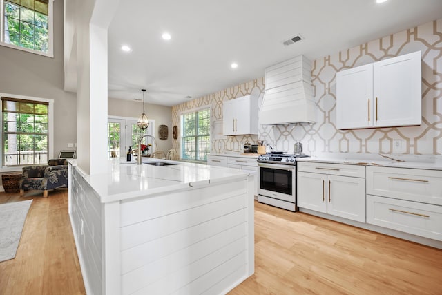 kitchen with a sink, stainless steel range with gas cooktop, recessed lighting, visible vents, and custom exhaust hood