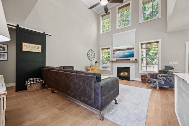 living area featuring ceiling fan, a barn door, light wood finished floors, a fireplace, and a towering ceiling