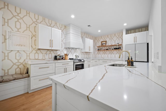 kitchen with stainless steel gas range oven, open shelves, a sink, custom range hood, and wallpapered walls