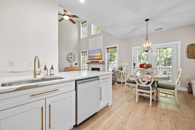 kitchen with ceiling fan, a warm lit fireplace, white cabinets, a sink, and dishwasher