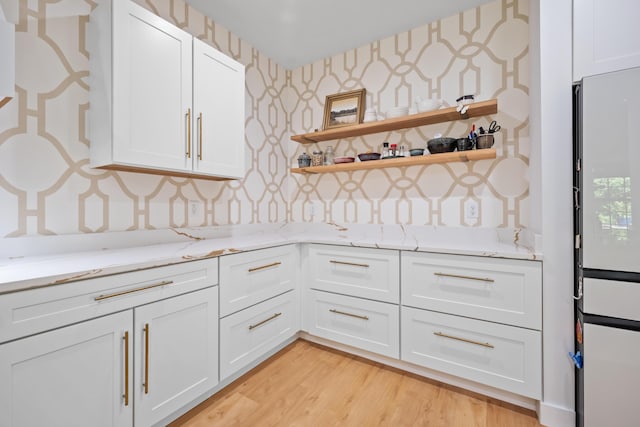kitchen featuring light stone counters, wallpapered walls, and white cabinetry
