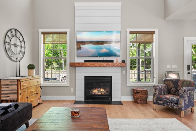 living room with a fireplace with flush hearth, baseboards, and light wood-style flooring