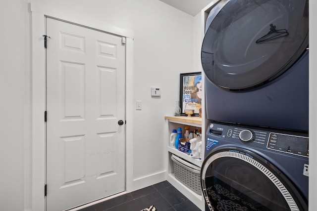laundry room featuring stacked washing maching and dryer, dark tile patterned floors, baseboards, and laundry area