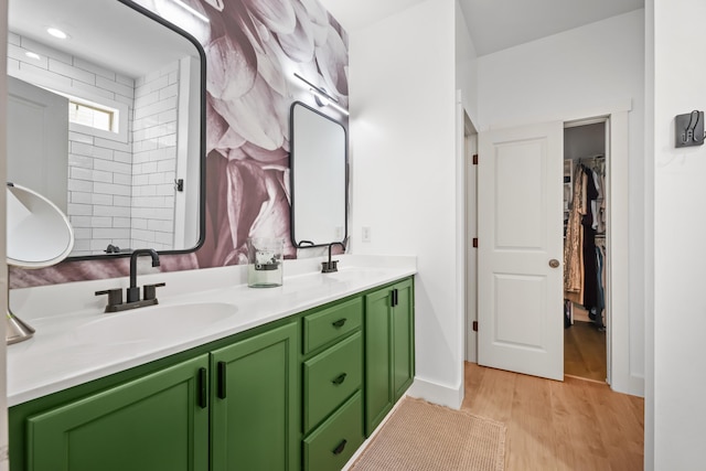 full bathroom with double vanity, a sink, a walk in closet, and wood finished floors