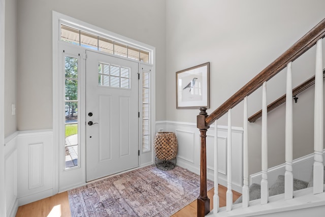 foyer entrance featuring stairway, a decorative wall, wainscoting, and wood finished floors