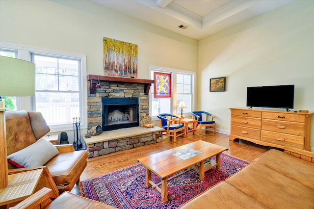 living room with a fireplace, wood finished floors, baseboards, visible vents, and ornamental molding
