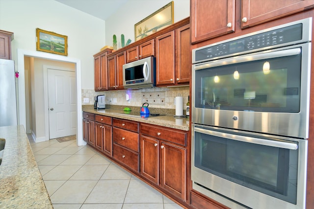 kitchen featuring light tile patterned flooring, appliances with stainless steel finishes, light stone counters, and decorative backsplash
