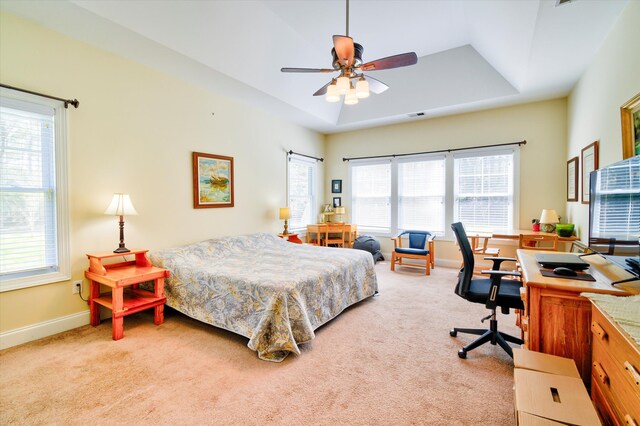 bedroom featuring a tray ceiling, baseboards, visible vents, a ceiling fan, and light carpet