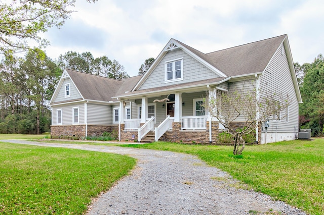 view of front of property featuring stone siding, central AC, a front yard, curved driveway, and a porch