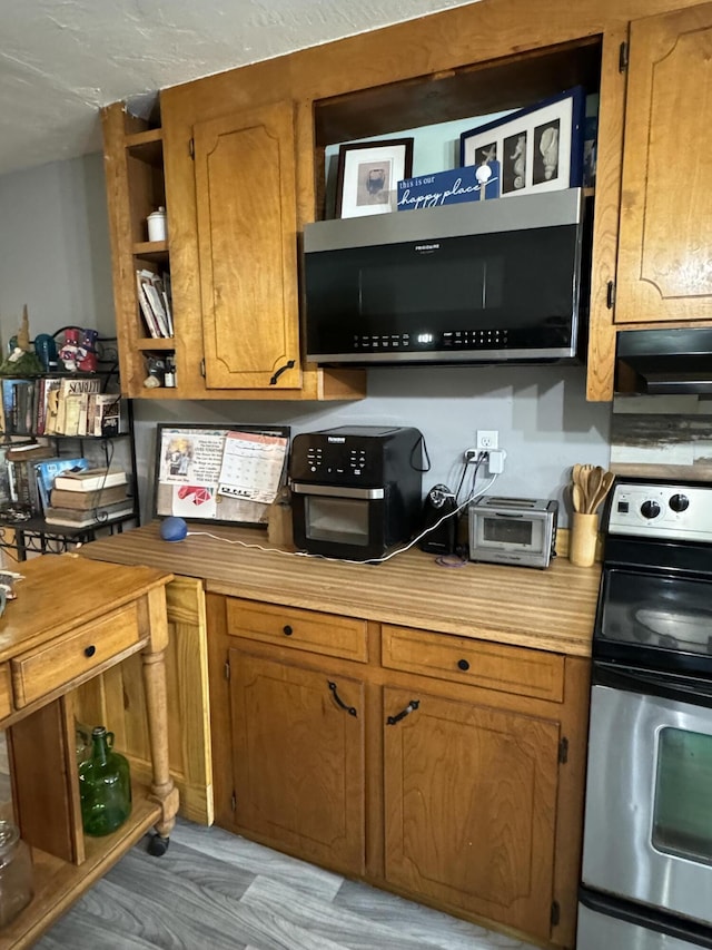 kitchen featuring light wood finished floors, open shelves, appliances with stainless steel finishes, brown cabinetry, and a toaster