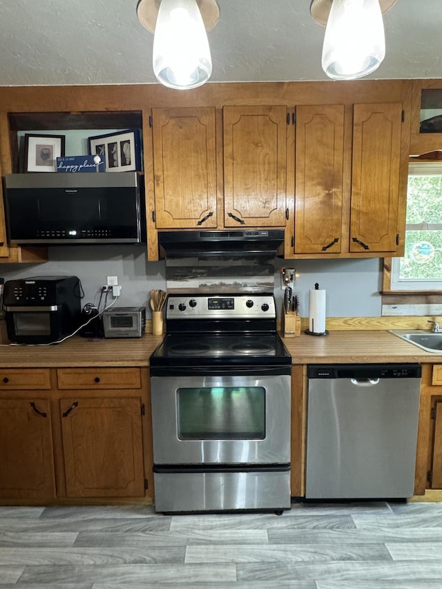 kitchen with under cabinet range hood, appliances with stainless steel finishes, light countertops, and brown cabinetry