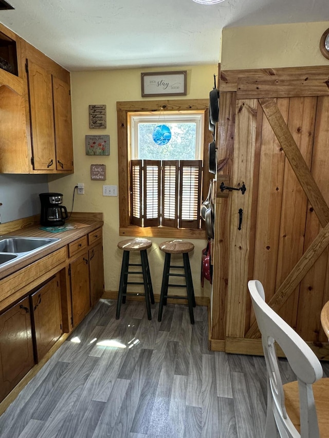 kitchen with a sink, baseboards, wood finished floors, and brown cabinetry