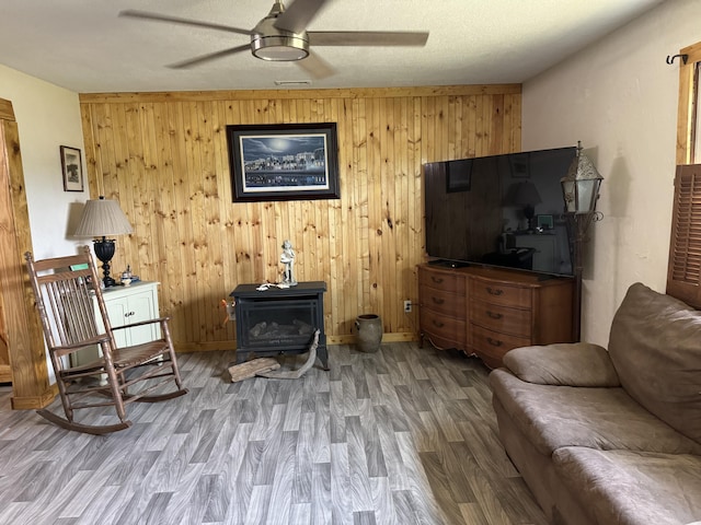 interior space with a ceiling fan, wood finished floors, baseboards, a wood stove, and wood walls