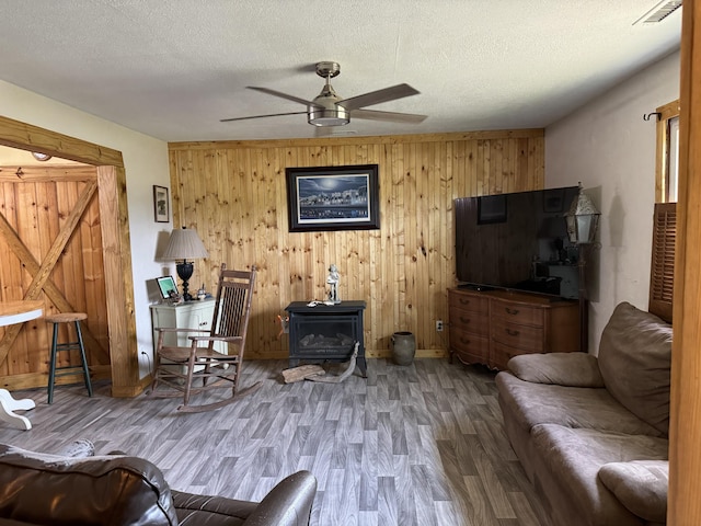 living room with visible vents, a textured ceiling, wood finished floors, ceiling fan, and a wood stove